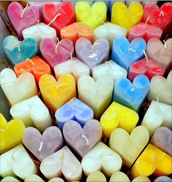 Attēlā redzamas no augšas nofotografētas krāsas sveces sirds formiņās.