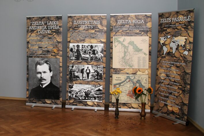 Attēli redzami banneri ar muzejpedagoģiskās programmas "Zelts" informāciju - "Zelta" laiks Andreja Upīša dzīvē, Ilustrētais "Zelts", Zelta Rīga, Zelts pasaulē. Banneri vertikāli izvietoti kabineta stūrī.