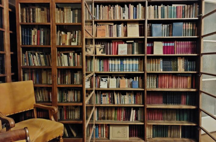 Grāmatu skapis Andreja Upīša viesistabā. Gar visu sienu atrodas grāmatplaukts, kas pilns ar grāmatām. Diviem plauktiem priekšā ir stikla durvis, divas citas durvis ir atvērtas. Kreisajā pusē priekšā grāmatām atrodas krēsls.