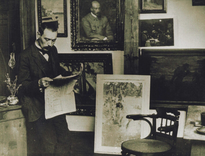 Vēsturiska fotogrāfija, kurā redzams mākslinieks Jānis Rozentāls, stāvot savā darbnīcā un lasot avīzi. Telpā redzamas vairākas gleznas — gan pie sienas, gan atbalstītas pret to. Mākslinieks ir tērpies tumšā uzvalkā ar tauriņkravatu, blakus redzama koka krēsla un galda mala ar vāzīti un ziediem. Telpai piemīt mākslinieciski iekārtota, radoša atmosfēra.